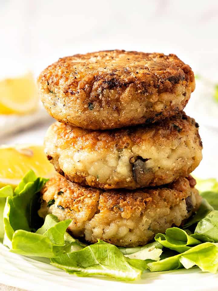 Close up stack of risotto cakes on lettuce leaf. White plate, lemon wedges, white background.