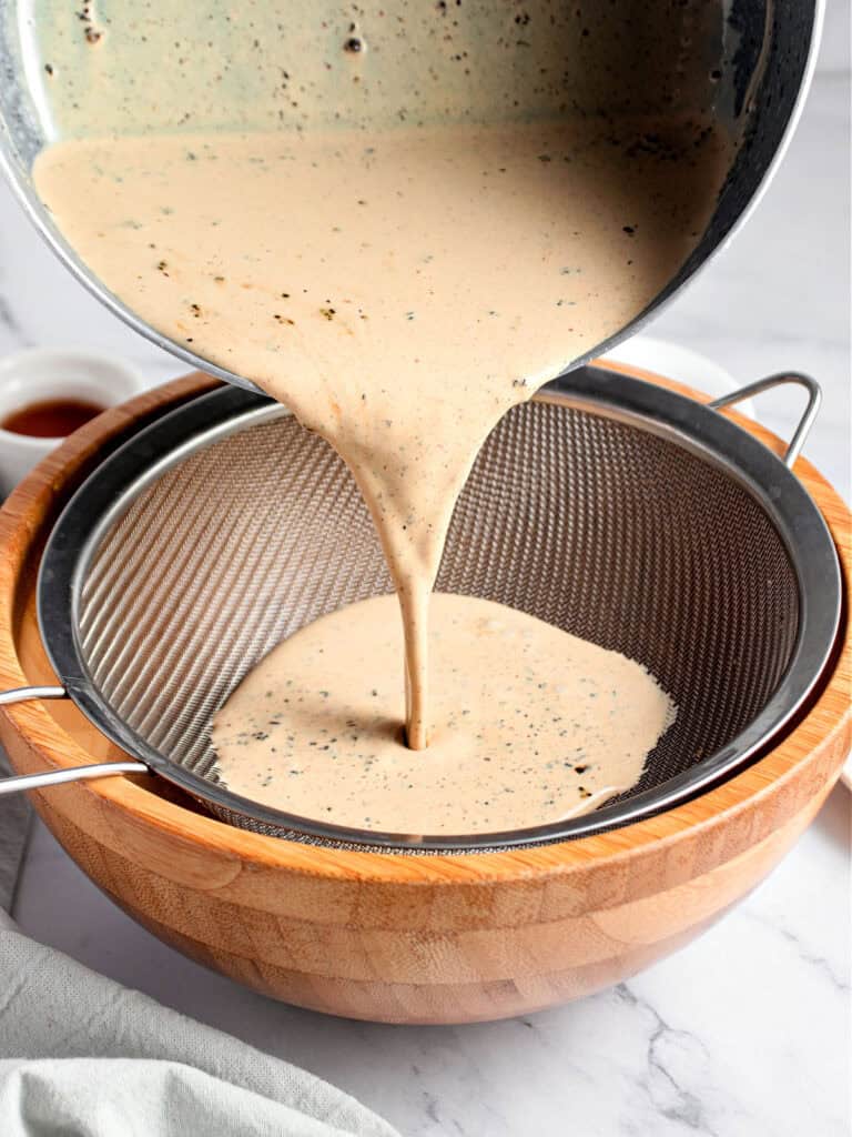 Coffee-infused milk being strained into a wooden bowl.