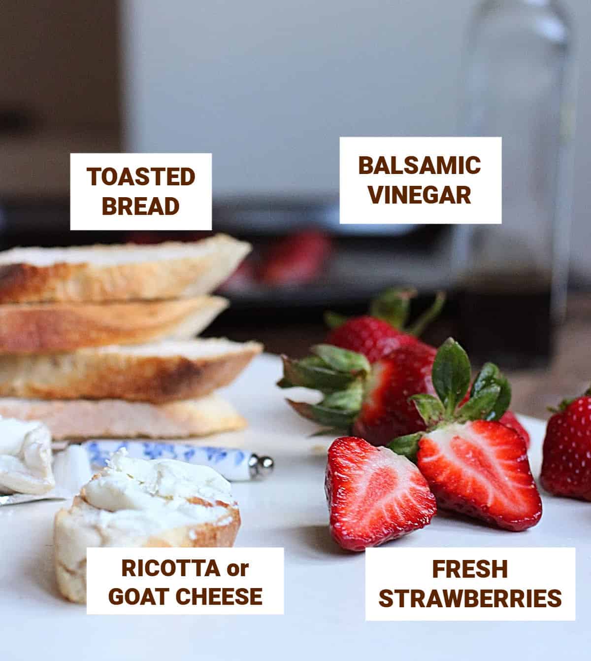 Strawberries, bread slices, vinegar bottle, cheese, knife on white table, text overlay