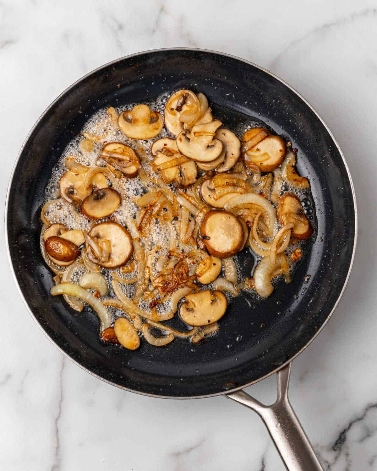 Mushrooms and onion cooked in a dark skillet. White marble surface.