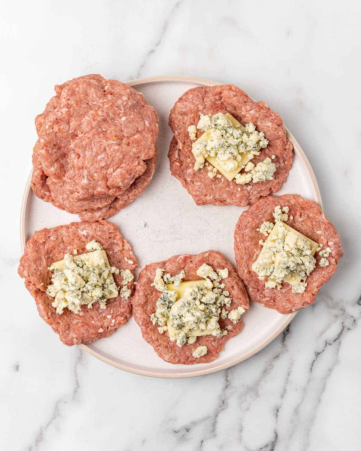 Meat patties with cheese on a white plate on a white and grey striped marble surface.