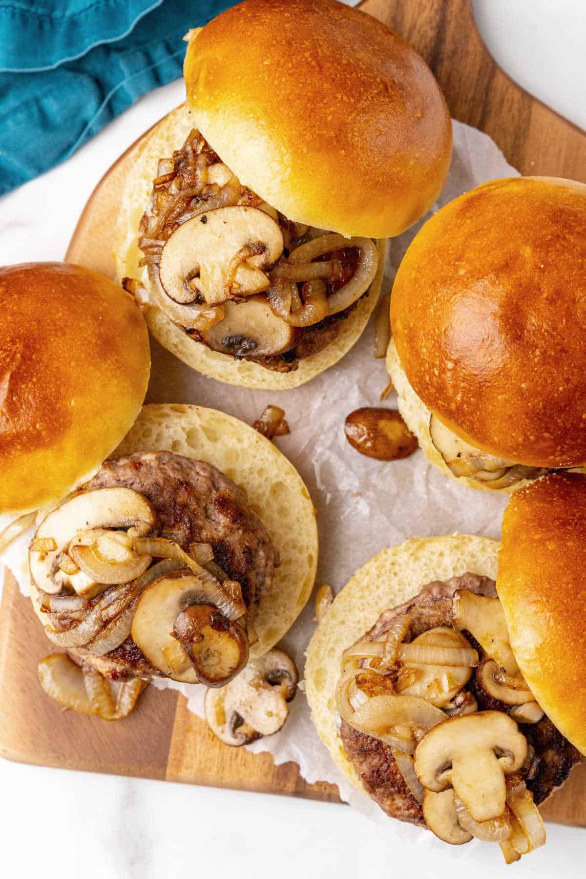 Several opened buns with burgers and mushroom topping on a wooden board. Top view. 