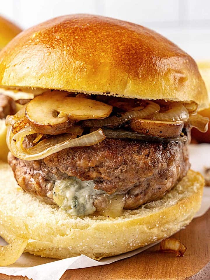 Burger with blue cheese stuffing and mushrooms on a golden bun. Wooden board and white background.