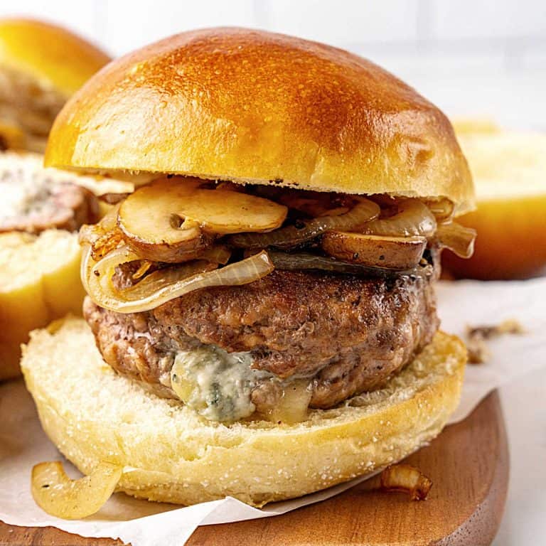 Burger with blue cheese stuffing and mushrooms on a golden bun. Wooden board and white background.