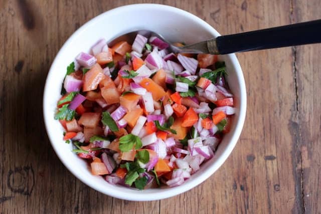 White bowl of salsa on wooden board.