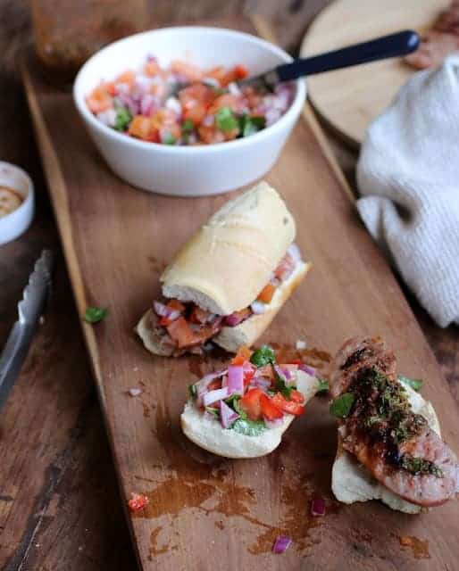 Chorizo, chimichurri and salsa sandwiches on wooden board, a white bowl with salsa..