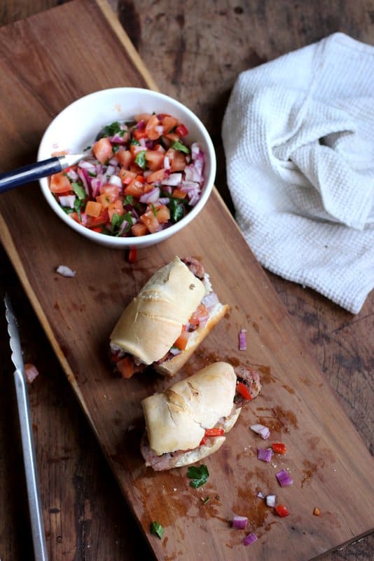 Chorizo, Chimichurri Sandwiches on wooden board, bowl of salsa, white kitchen towel