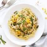 Top view of white plate with asparagus corn pasta. White surface.