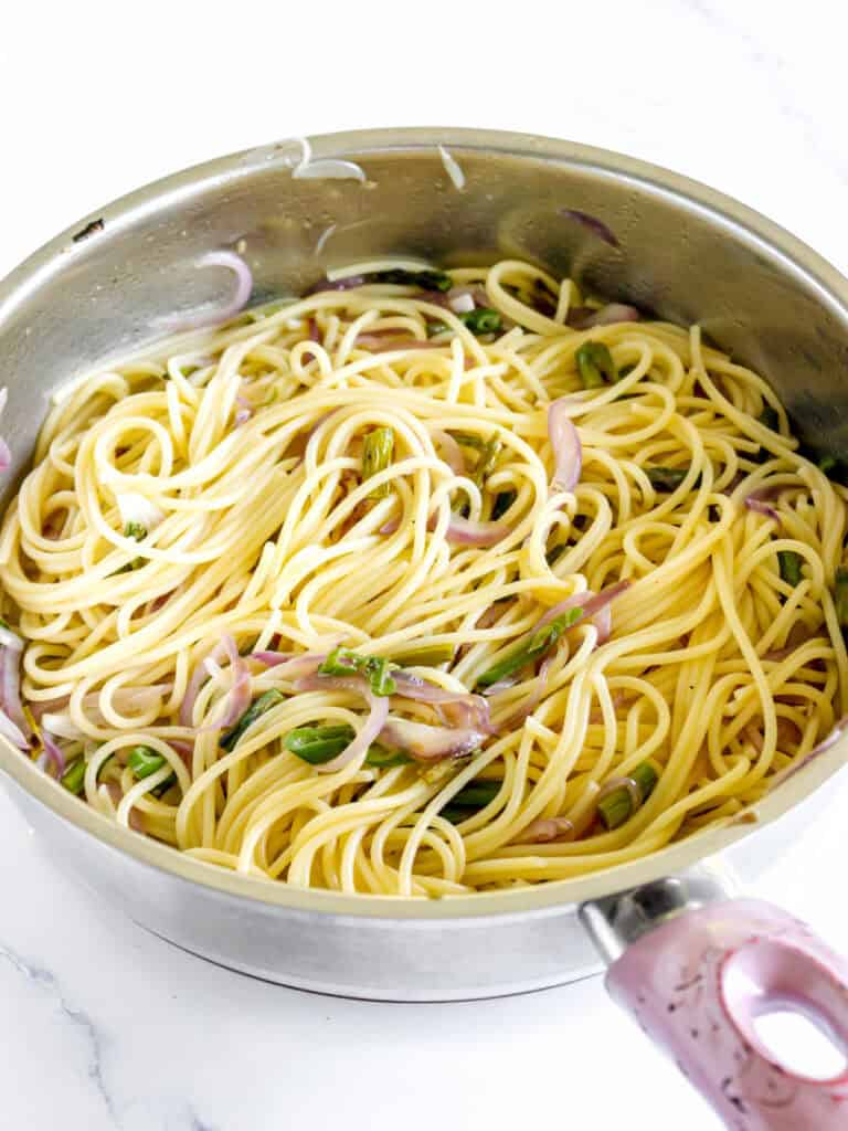 Metal skillet with spaghetti, asparagus and onion. White surface.