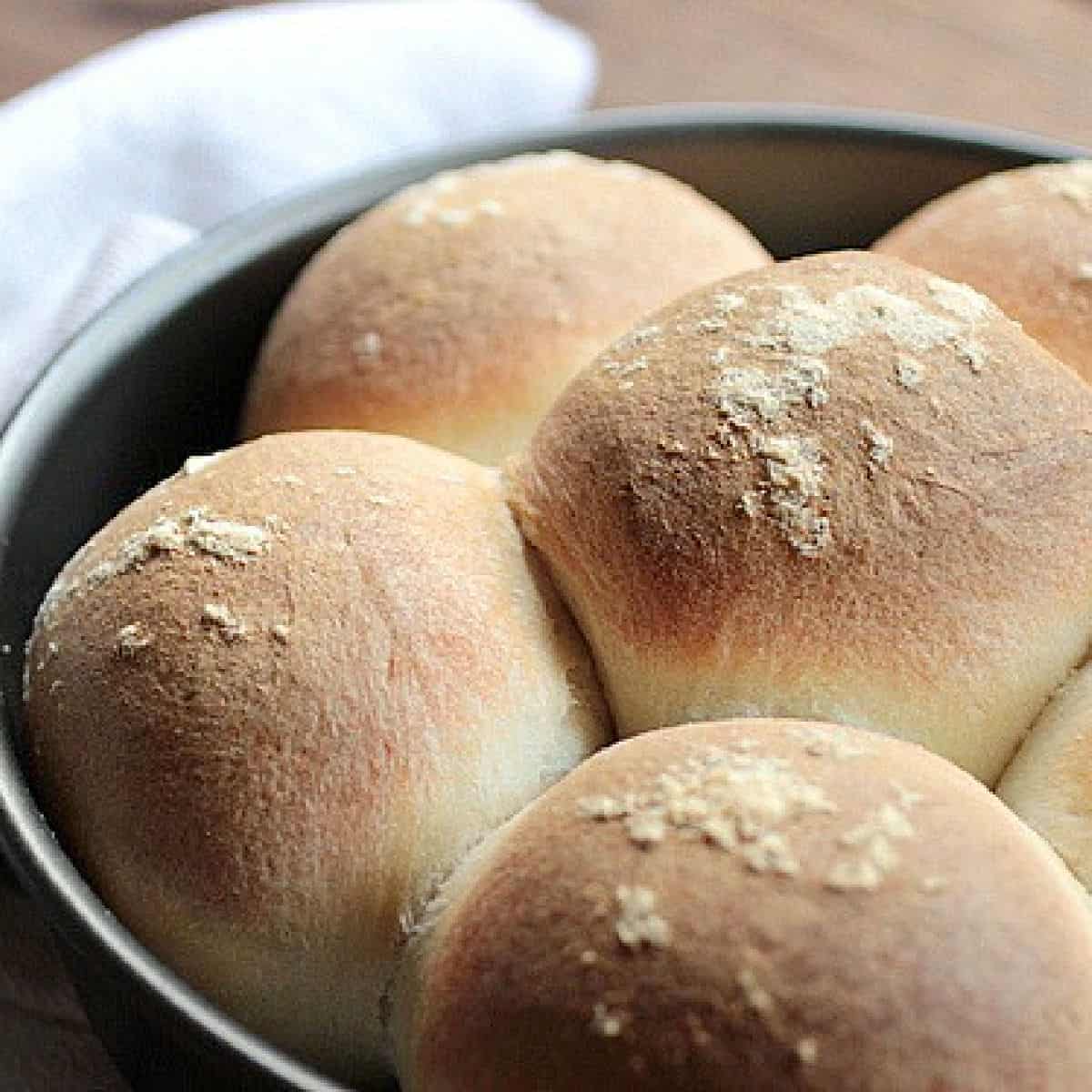 Metal pan with freshly baked rolls on wooden table, a kitchen towel.