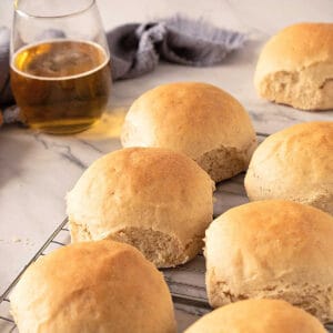 Two rows of dinner rolls on a white marbled surface. Glass of beer and kitchen towel in the background.