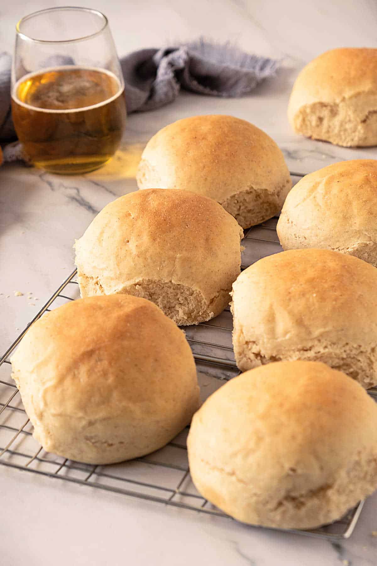 Two rows of beer dinner rolls on a wire rack. White marbled surface. Glass of beer in the background. 
