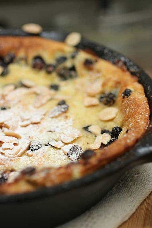 Cast iron skillet with almond covered blueberry pancake in a black skillet.