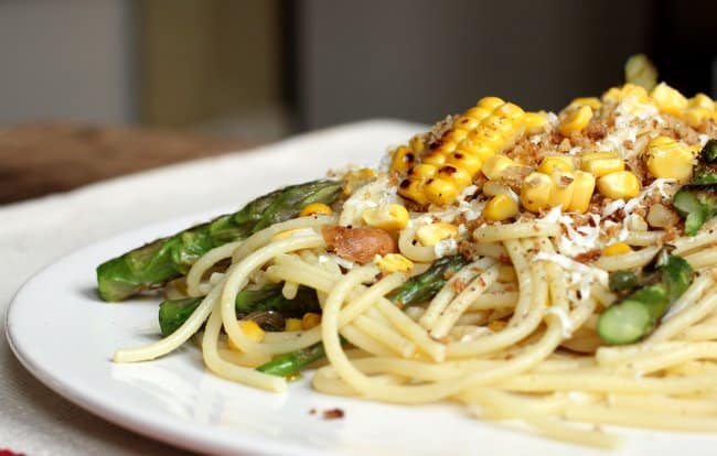 Side view of spaghetti with corn and asparagus on a white plate