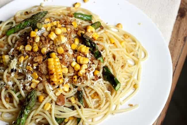 White plate featuring pasta with corn and asparagus 