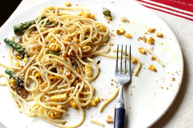 Half eaten spaghetti with corn and asparagus on a white plate with a fork
