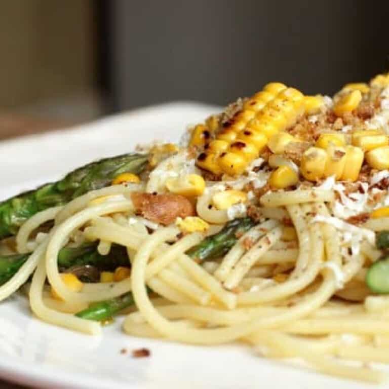 Partial view of white plate with corn asparagus spaghetti.