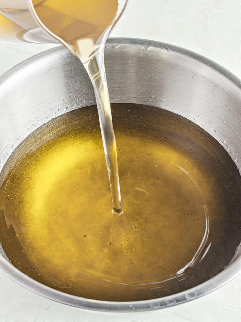 Adding syrup to lemon liqueur mixture in a metal bowl.