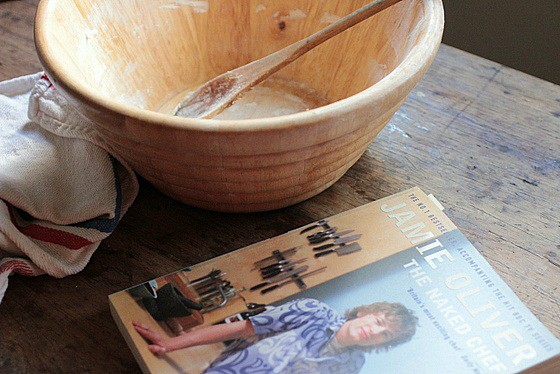 Wooden bowl with spoon on wooden table, a cookbook and kitchen towel