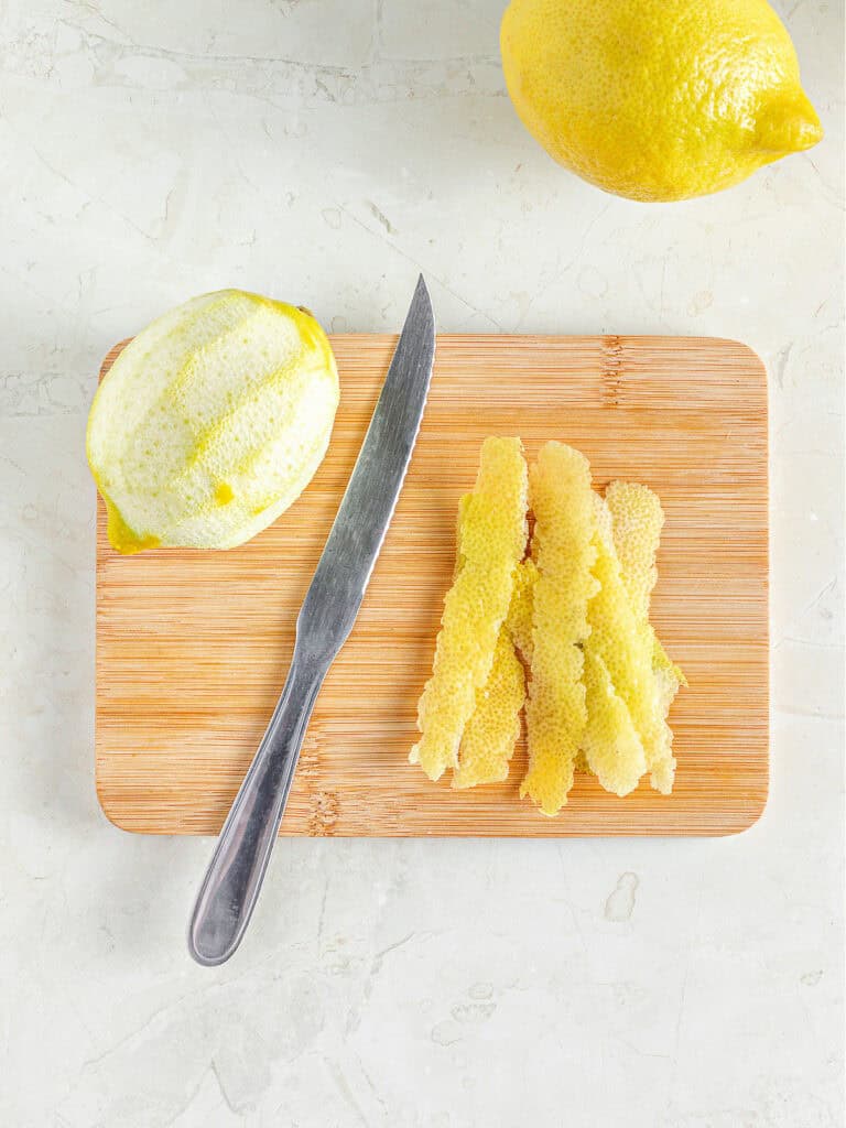 Wooden board with peeled lemon, lemon peel and knife. Gray surface.