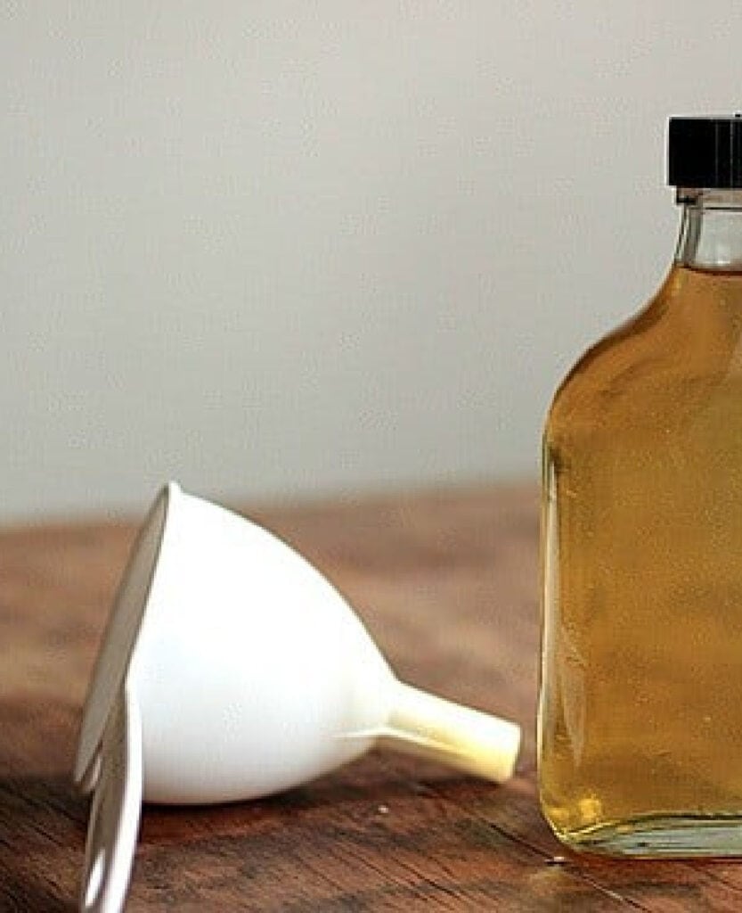Bottle with limoncello and white funnel on a wooden surface.