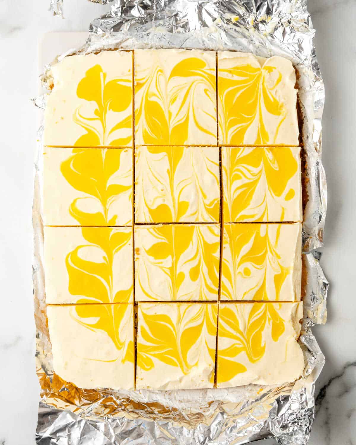 Cut squares of a rectangular passionfruit cheesecake on aluminum paper.