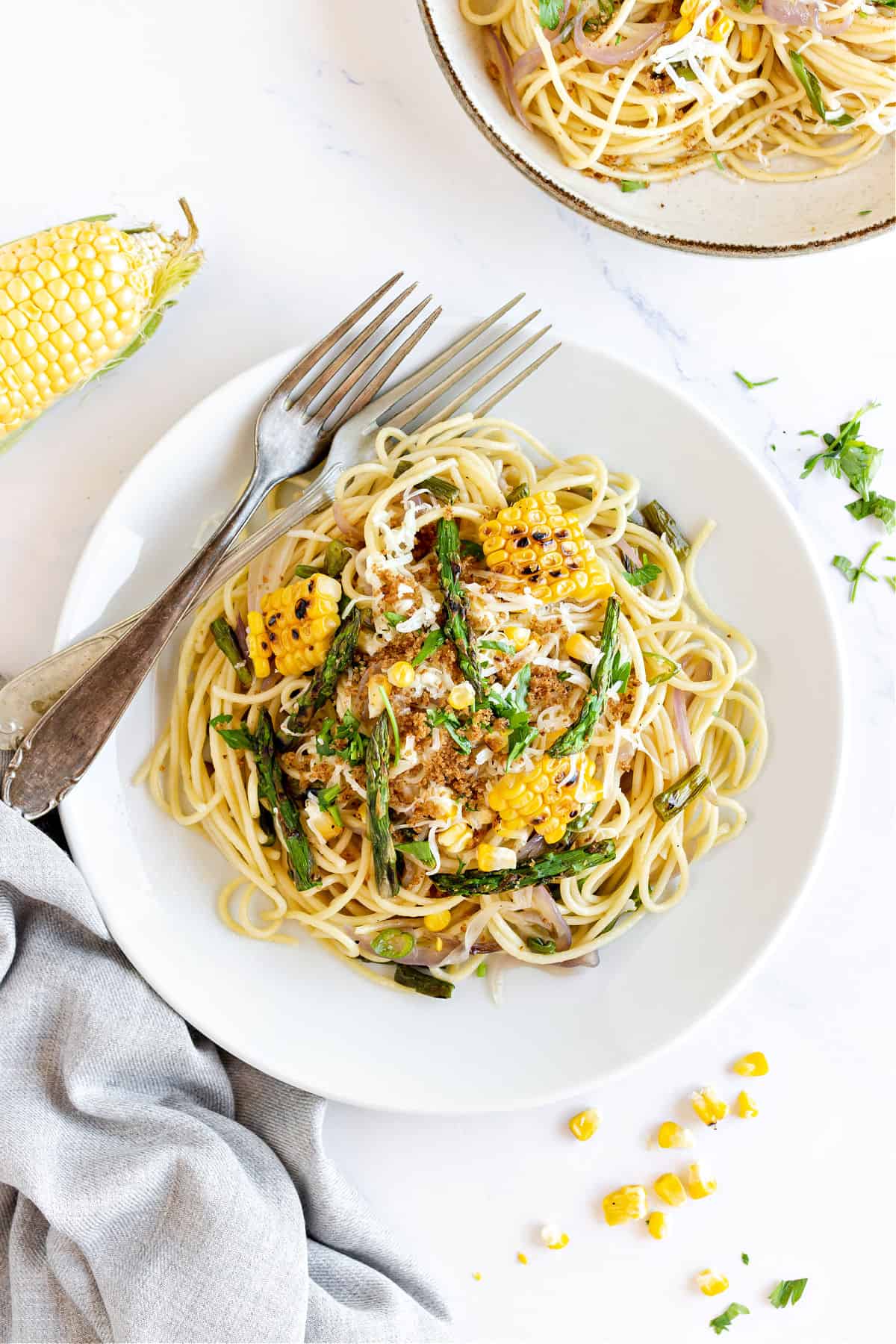 White plates with asparagus corn spaghetti. White background. Silver forks.