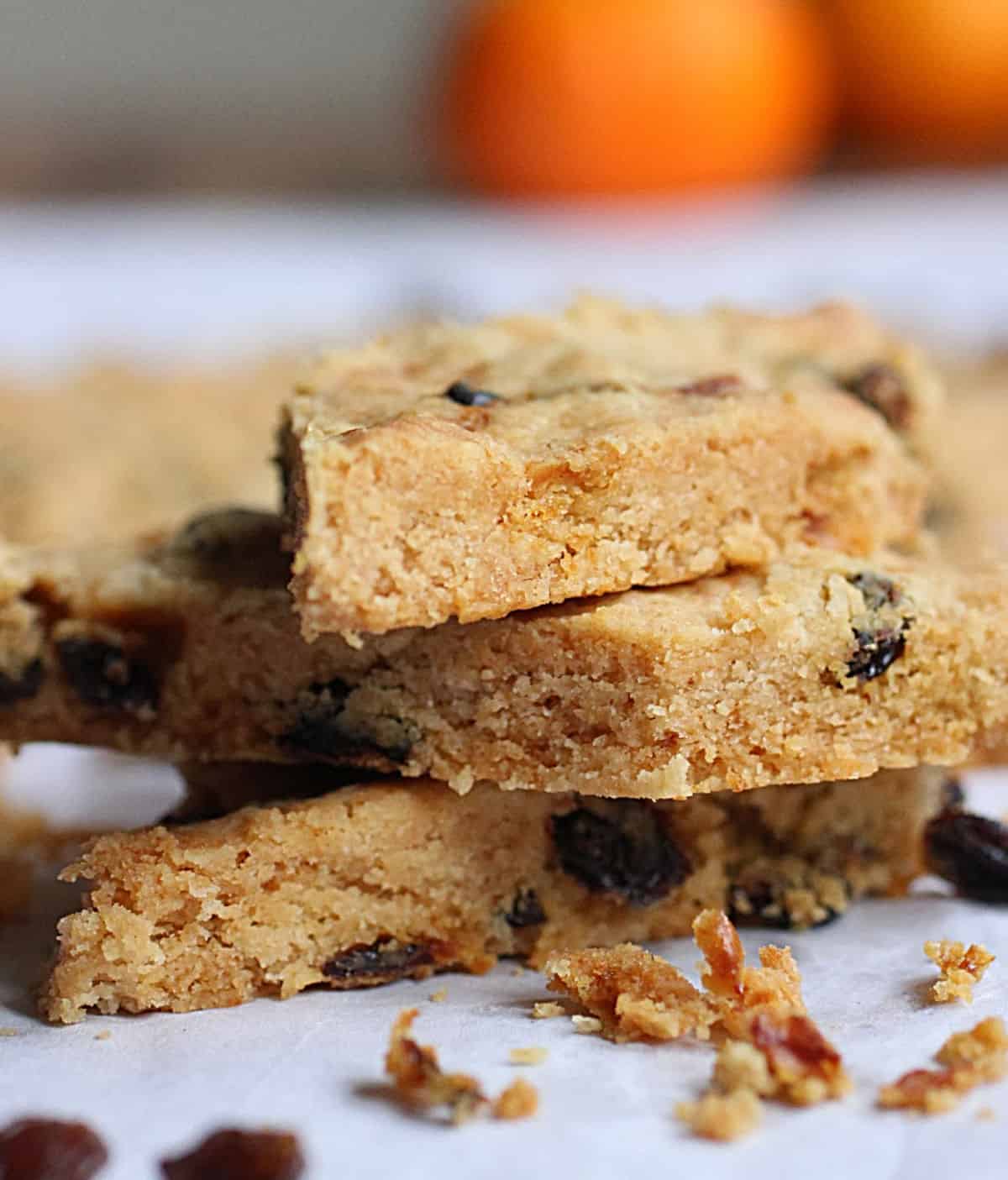 Stack of three pieces of raisin shortbread on a white paper. Oranges in the background.