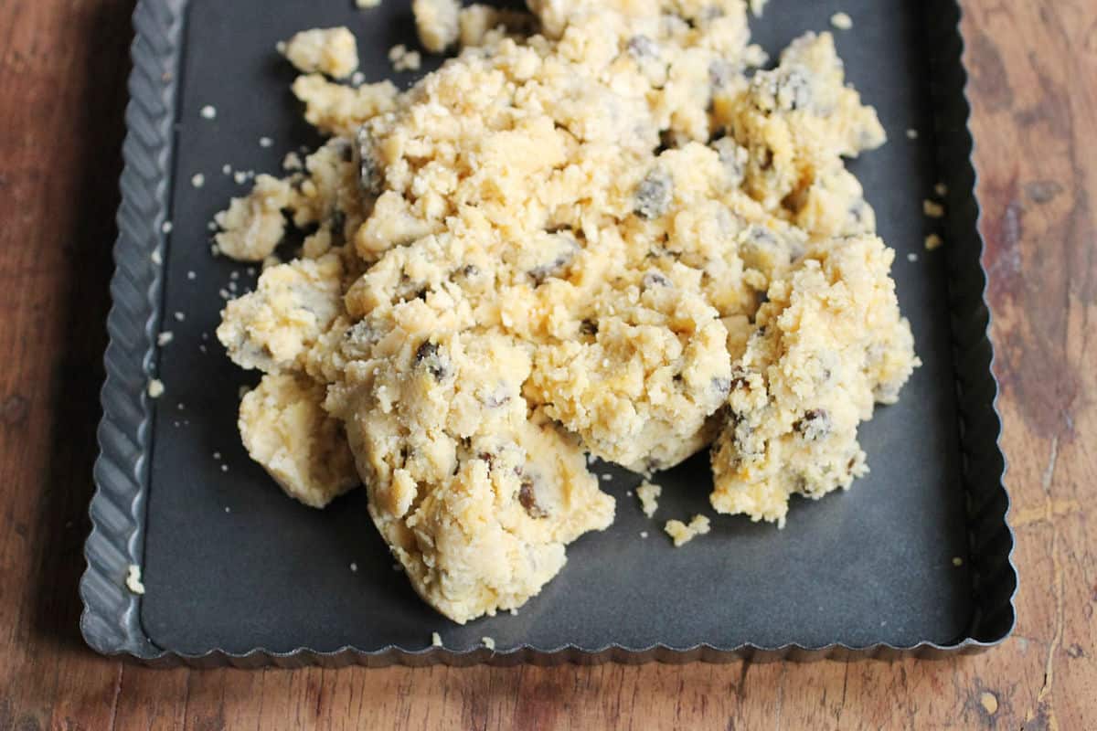 Dark metal square pan on a wooden table with raisin shortbread dough.