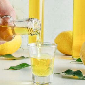 Close up image of limoncello shot being poured. Grey background, liqueur bottles.