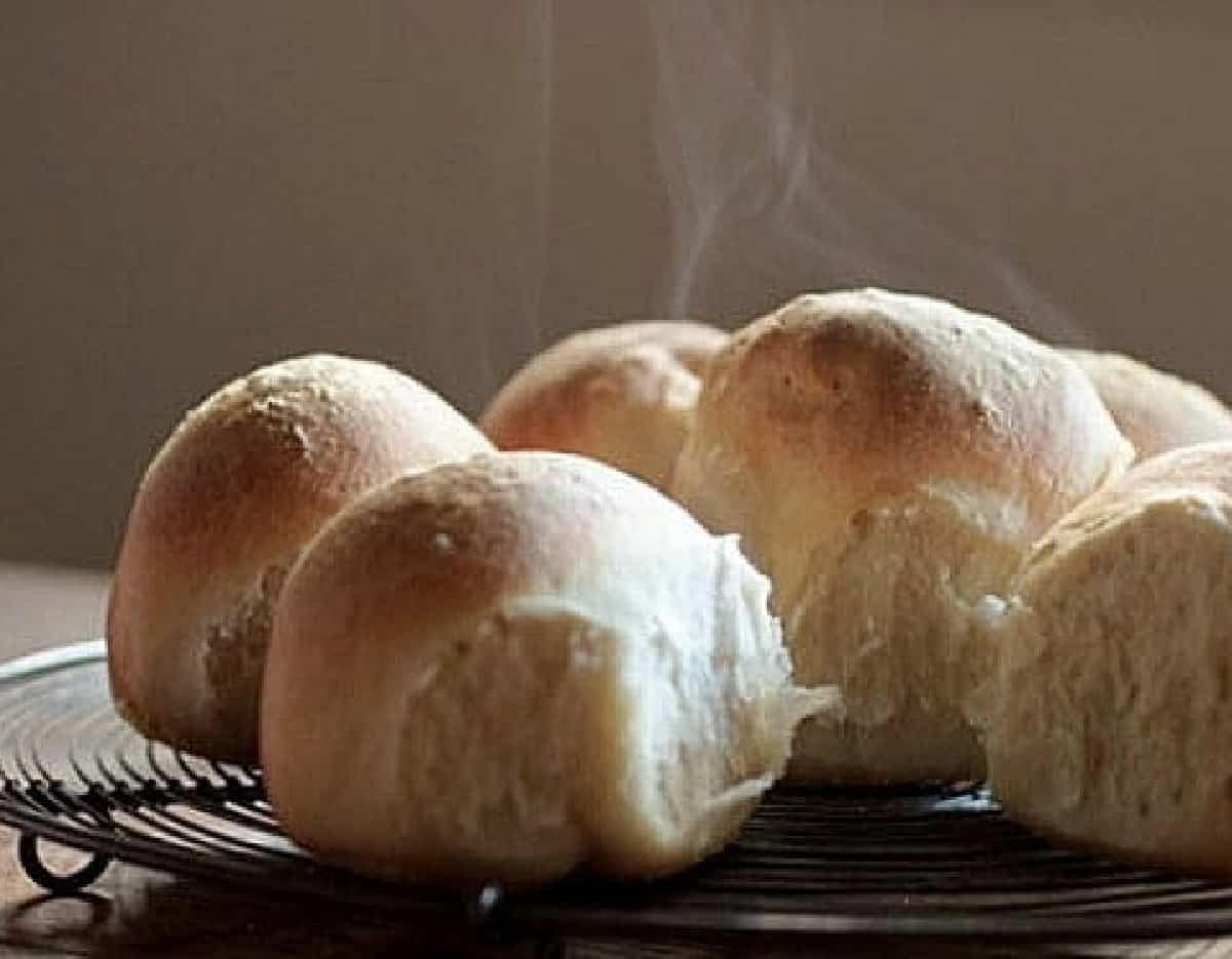 Warm steaming bread rolls on wire rack.