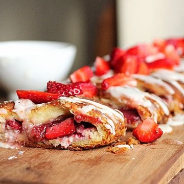 Strawberry danish braid on wooden board, white bowl in background, fresh strawberries on top