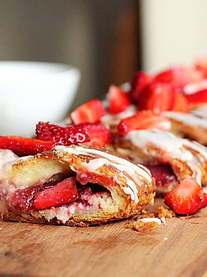 Strawberry danish braid on wooden board, white bowl in background, fresh strawberries on top
