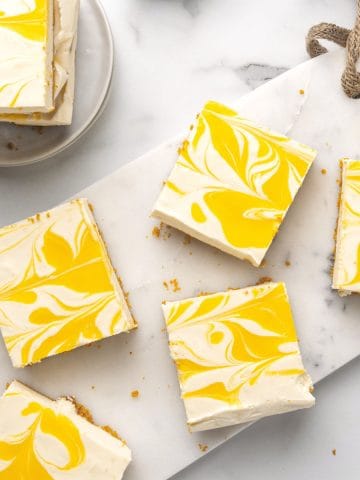 Several squares of passion fruit cheesecake on a white marble surface. View from above.