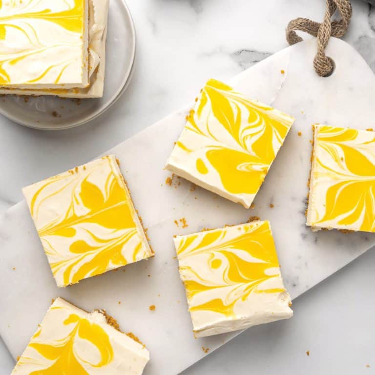 Several squares of passion fruit cheesecake on a white marble surface. View from above.