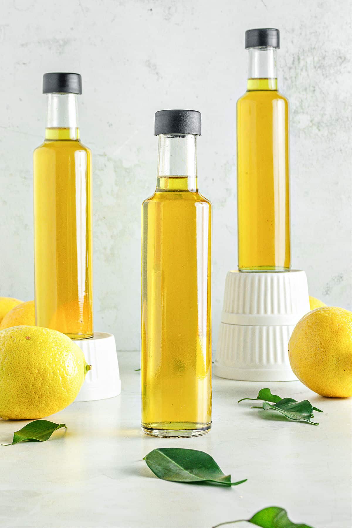 Three thin bottles of limoncello, gray background, lemons and lemon leaves.