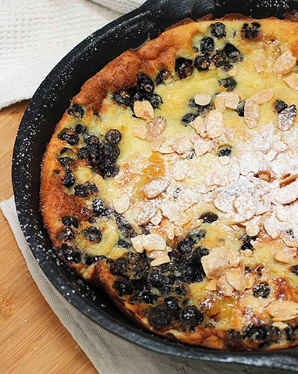 Cast iron skillet with baked blueberry pancake, almonds on top and powdered sugar. 