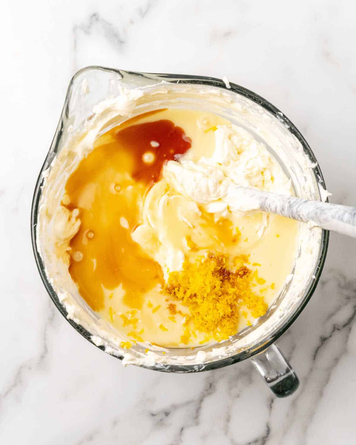 Cheesecake batter with flavorings in a glass jar on a white and grey marble surface.