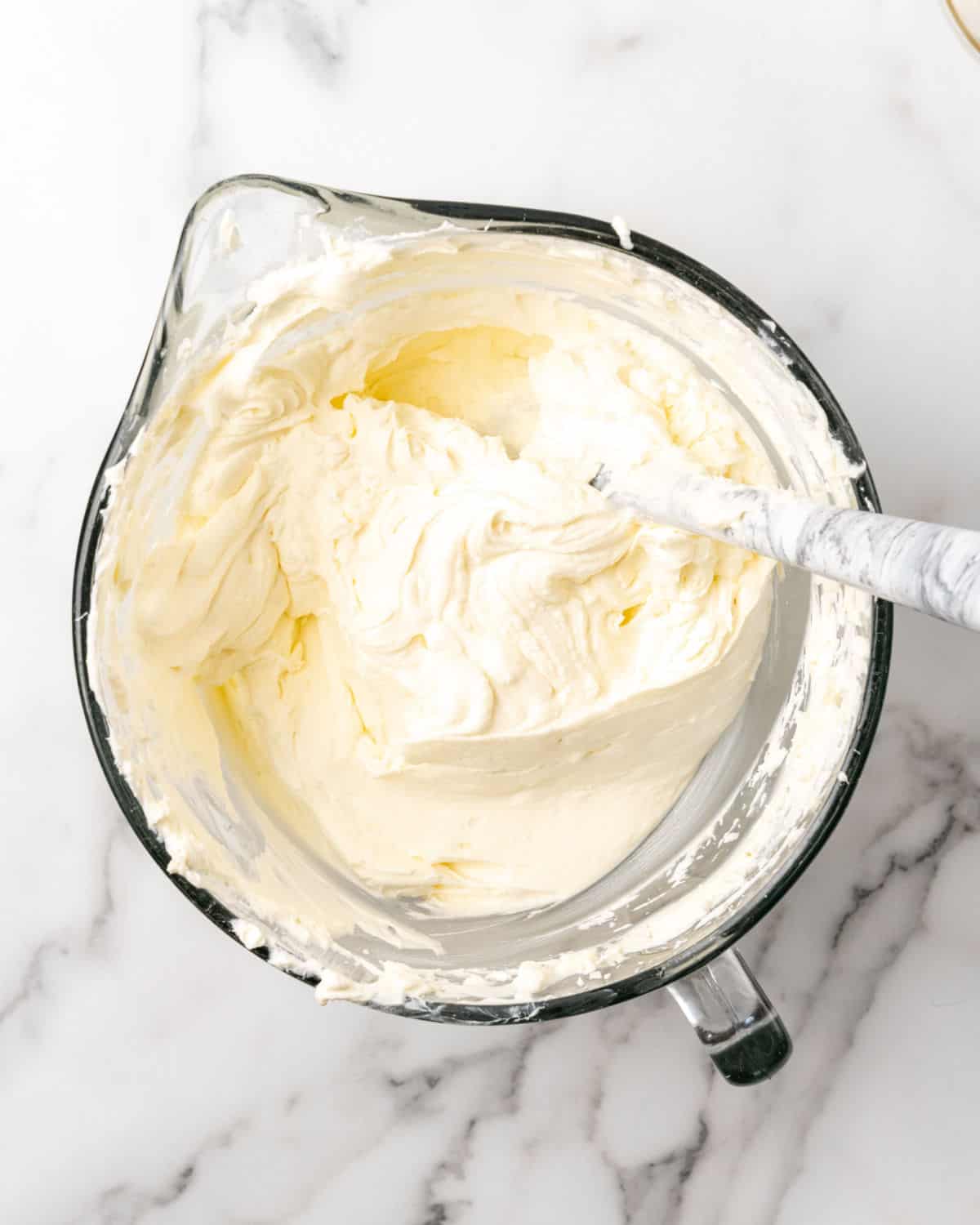 Cream cheese mixture for cheesecake in a glass bowl on a white marble surface.