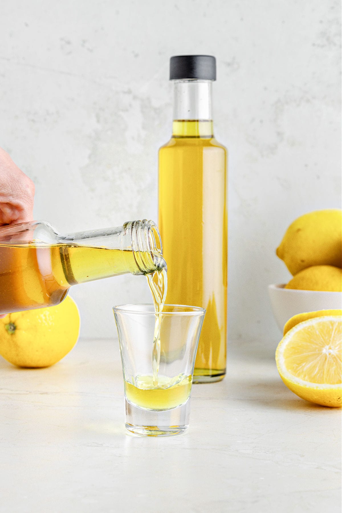 Serving a shot of limoncello. Lemons and bottle in gray background.