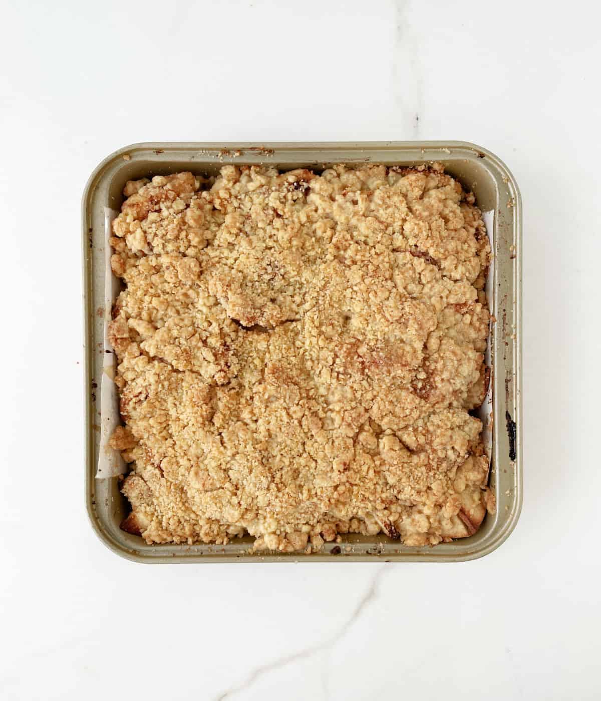 Top view of square pan with apple crumble on a white marble surface.