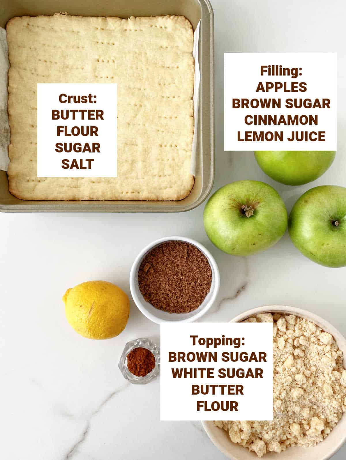 White marble with ingredients for apple crumb bars including shortbread crust in pan, streusel topping, lemon, cinnamon, brown sugar.