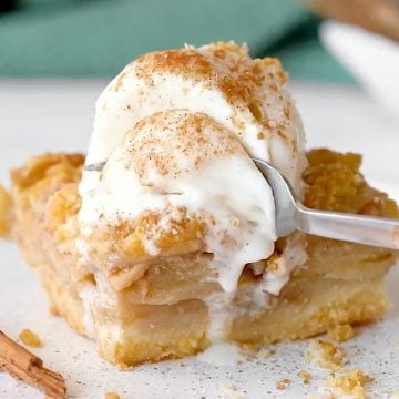 White plate with square of apple crumb bar with ice cream. Green cloth in the background.