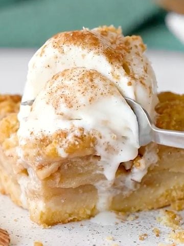 White plate with square of apple crumb bar with ice cream. Green cloth in the background.