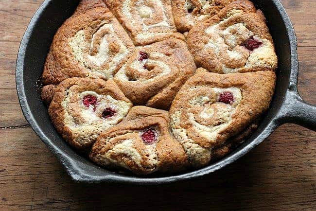 Dark skillet with raspberry rolls on a wooden surface. 