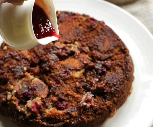 Raspberry sauce being poure over cinnamon rolls on a white plate. 