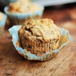 Open paper liner with banana chocolate chip muffin on a wooden table.