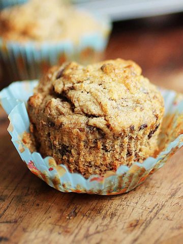 Open paper liner with banana chocolate chip muffin on a wooden table.