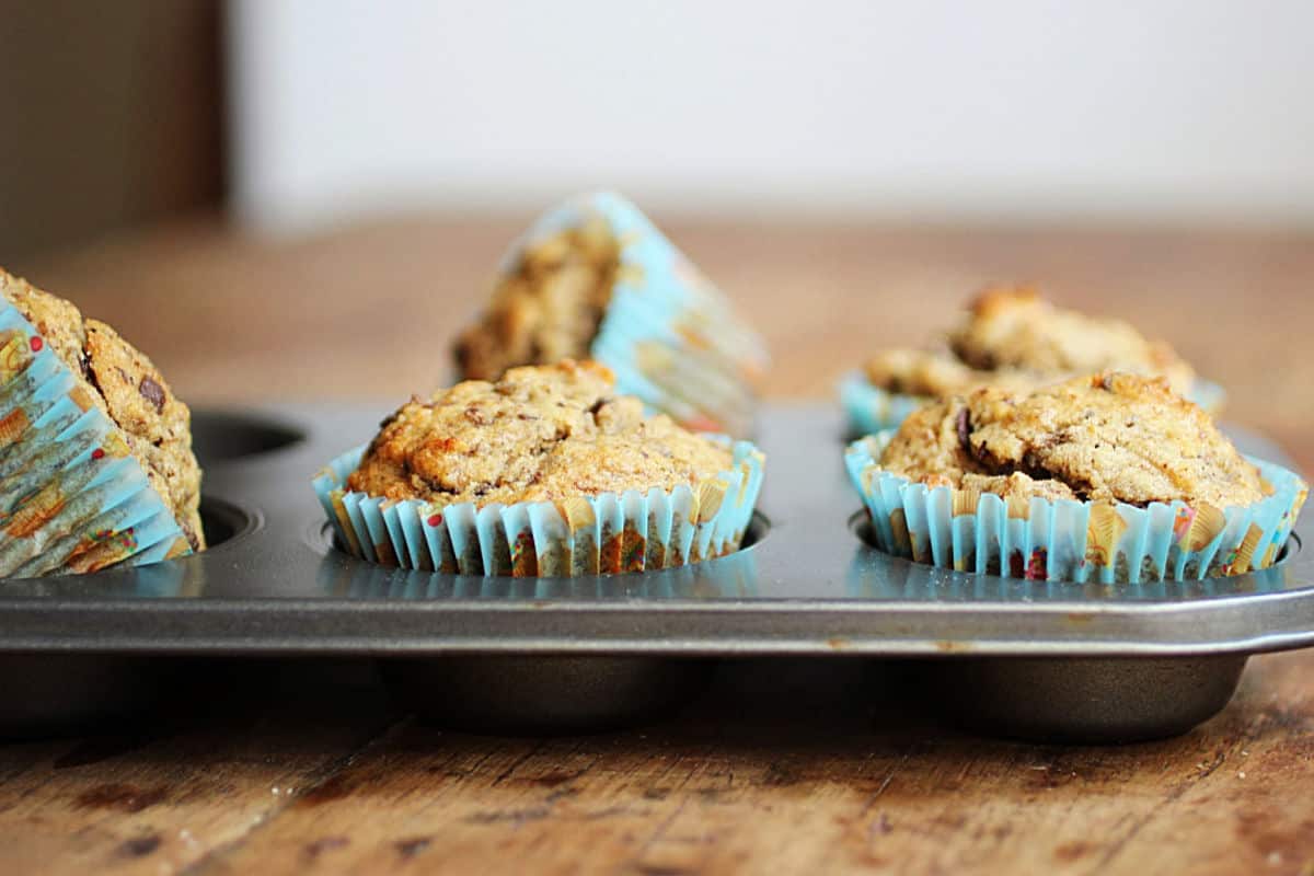 Metal pan with banana muffins in bluish paper liners on a wooden table. 