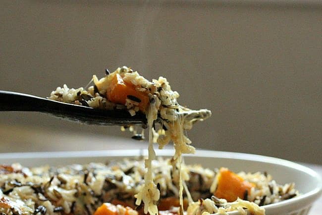 Wooden spoon lifting cheesy portion of rice and squash casserole